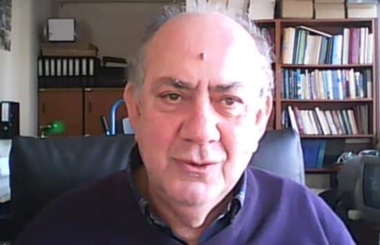 Photo of Theodore Chadijpadelis, a white man with grey, receding hair. We can see his head and shoulders. He appears to be talking and is sitting on a black leather chair. In the background, a bookshelf and a file cabinet.