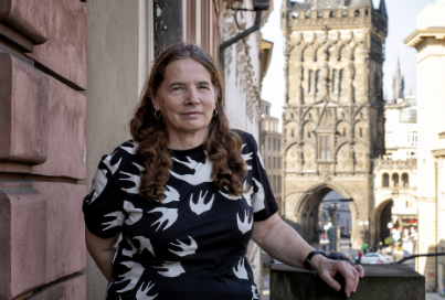 A photo of Martina Klicperová-Baker standing in front of a medieval tower.